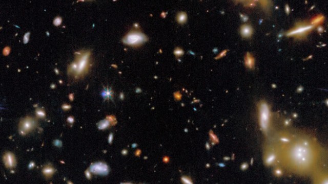 A view of deep space showing numerous galaxies of various shapes and sizes scattered across a dark background.