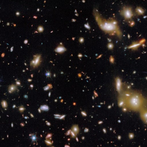 A view of deep space showing numerous galaxies of various shapes and sizes scattered across a dark background.