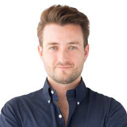 A man with light brown hair and blue eyes wearing a dark blue button-up shirt, standing against a white background, looking directly at the camera.
