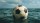 A black and white soccer ball floats on the surface of the ocean under a partly cloudy sky.