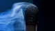 Close-up of a burnt matchstick with smoke swirling around its charred tip against a dark background.