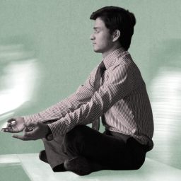 Scott Britton, in business attire, sits cross-legged on a desk meditating, while blurred figures move in the background.