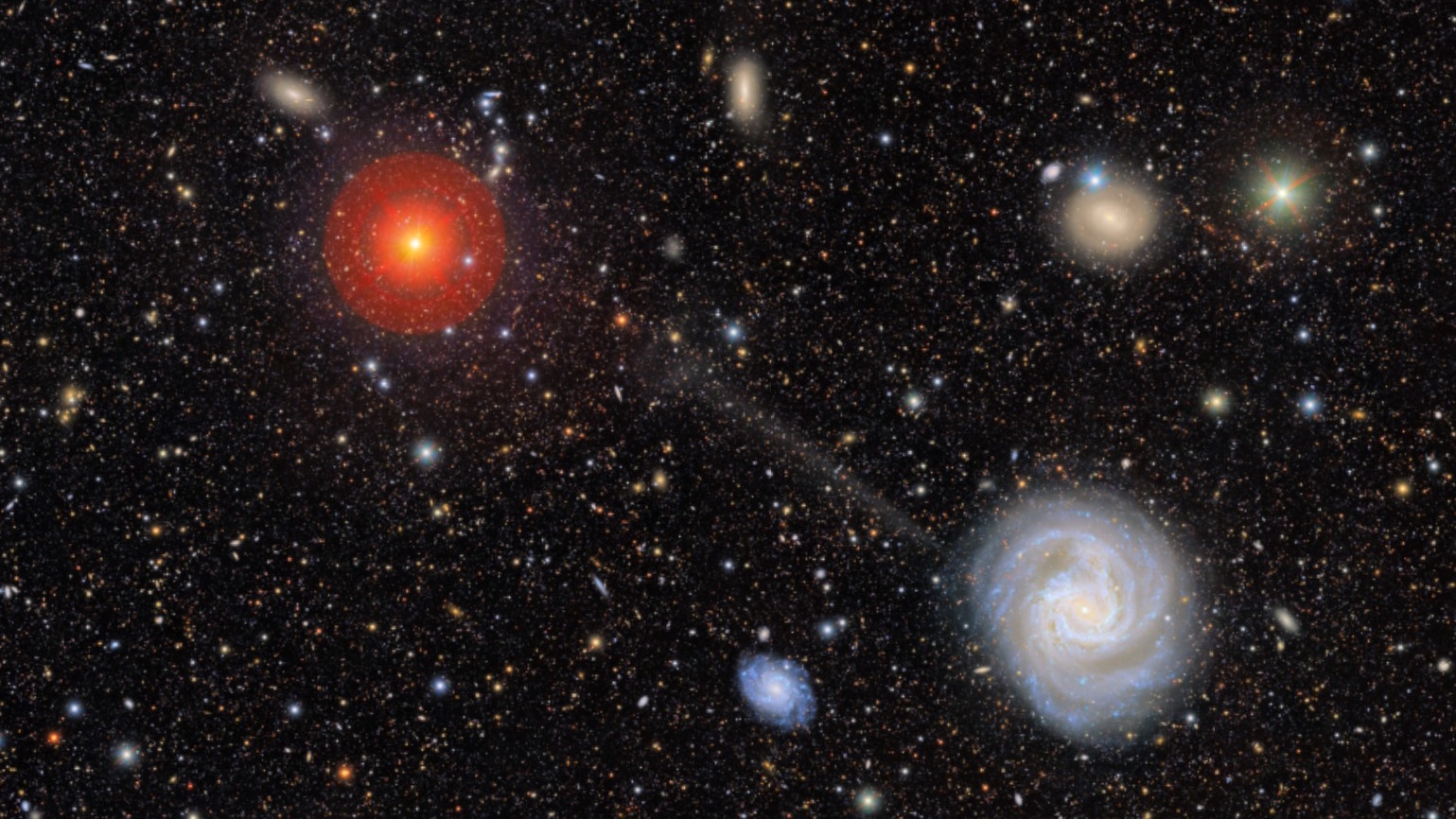 A field of galaxies in deep space, featuring a bright spiral galaxy at the lower right with a stellar stream escaping the galaxy, and a large, bright red star at the upper left.