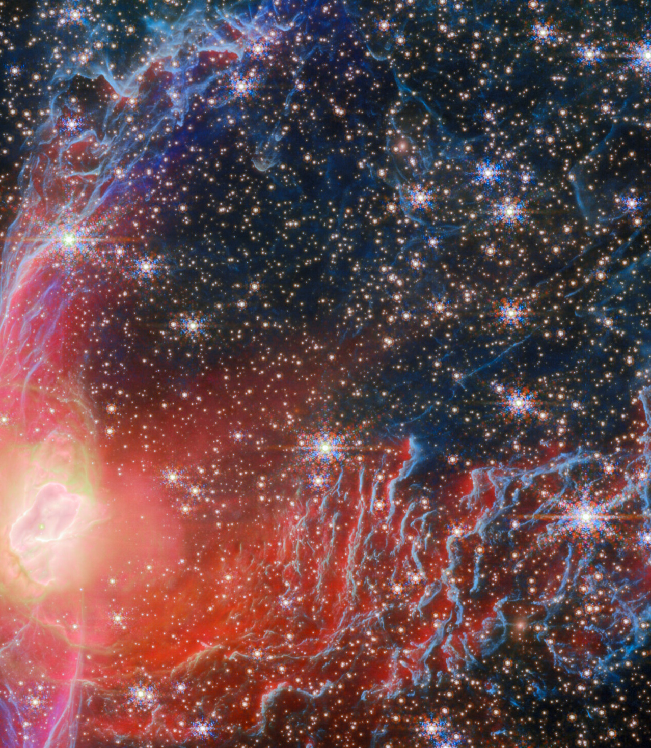 Image of a colorful nebula in space, showing a dense field of stars, bright red and blue gas clouds, and intricate light patterns.